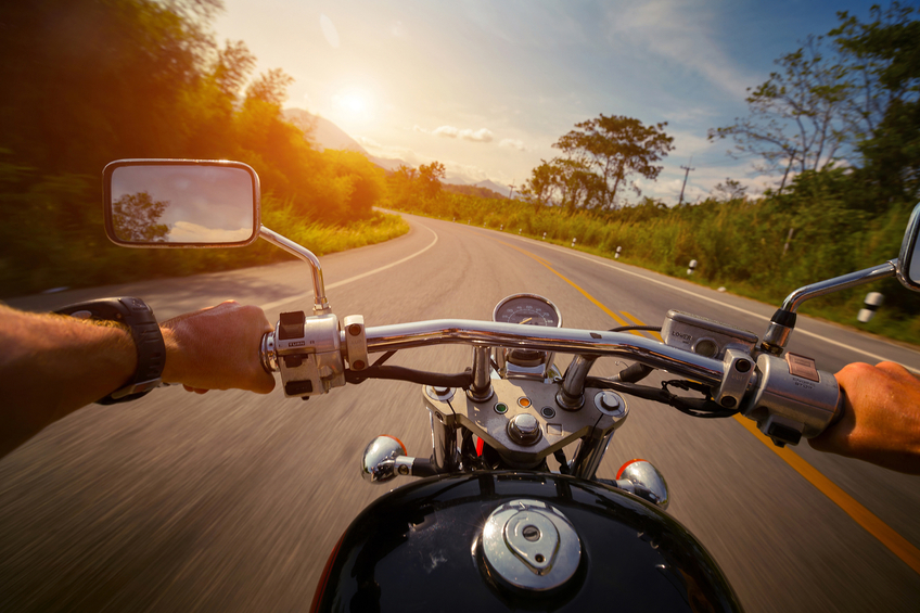 Driver riding motorcycle on the empty asphalt road into the sunset.