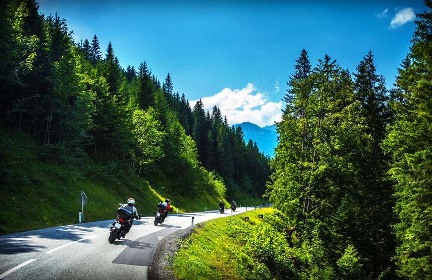 Motorcyclers riding down a wooded highway.