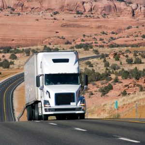 Image of a semi truck driving down a desert highway. 