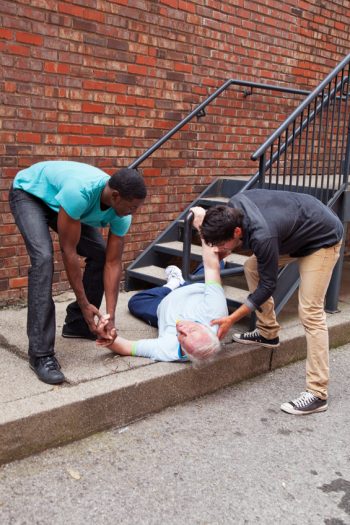 Two men helping a man after he fell down a set of stairs.
