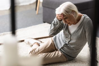 Elderly woman holding her head in pain while being on the floor