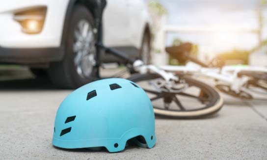 bike helmet and a bike laying on the road with a car passing by. 