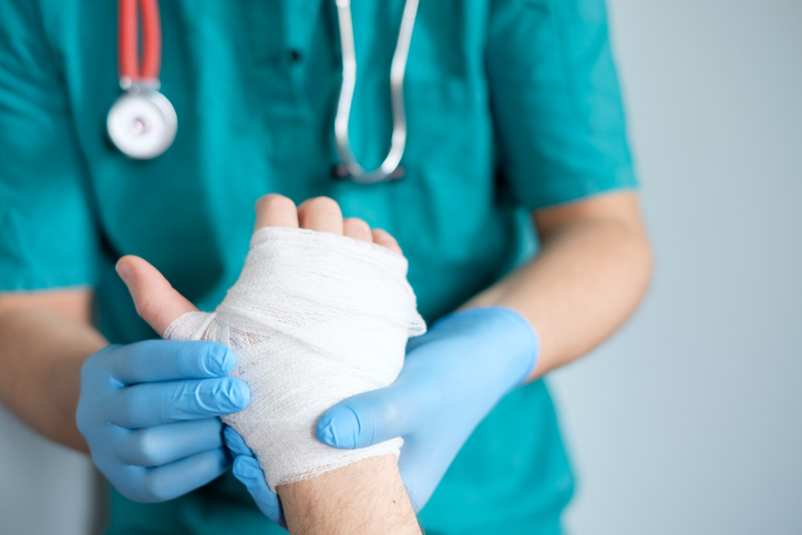 Doctor treating an injured hand which is wrapped in gauze bandage.