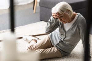 Elderly woman holding her head looking confused while on the ground