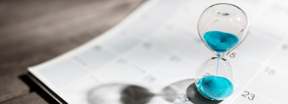 An hourglass with blue sand running through it sitting on a calendar