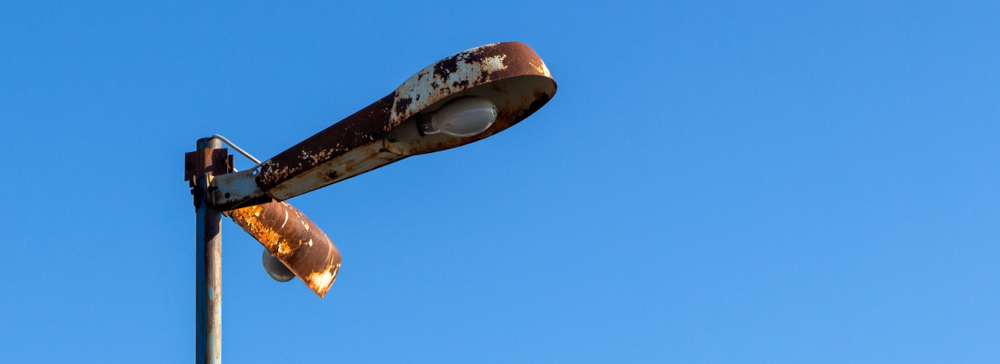 Lamppost with rusty shades with burnt out lamps against the blue sky.