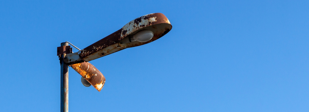 Lamppost with rusty shades with burnt out lamps against the blue sky. 