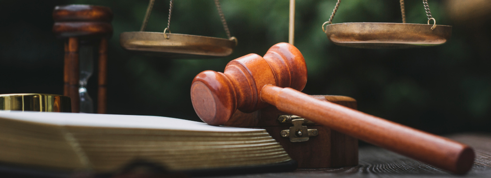 A gavel lying on top of an open legal book with scales of justice in the background