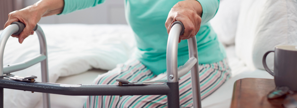 Close-up picture of an elderly woman with a walker getting up off a bed