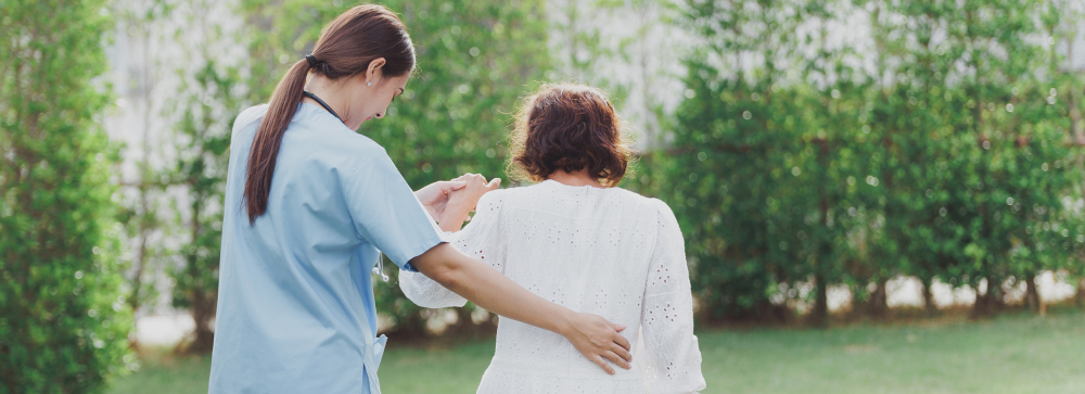 An attendant at a nursing home helps a resident walk through a garden