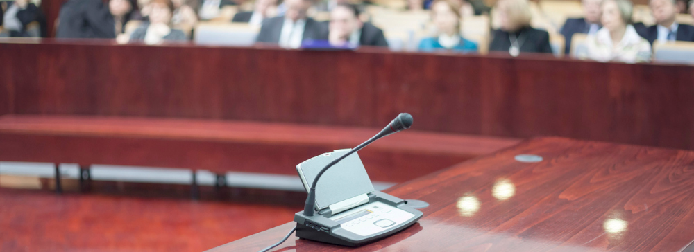 A microphone on a counsel table in a courtroom with people in the gallery