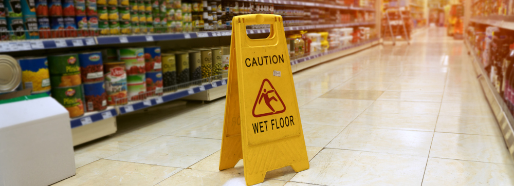 A yellow "caution: wet floor" sign in the aisle of a supermarket