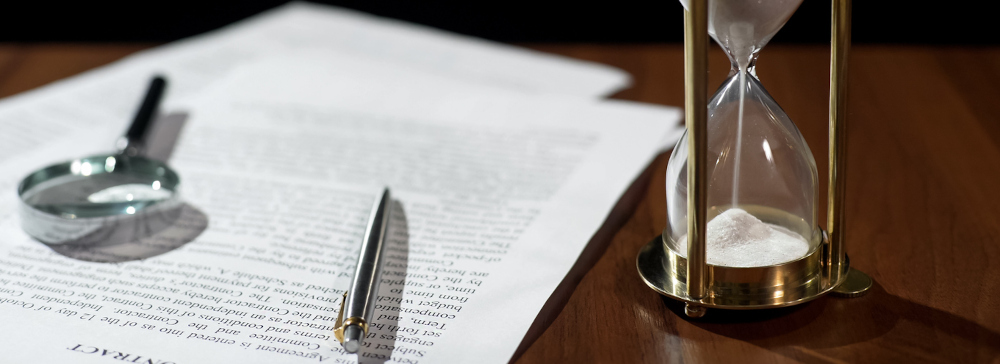 A legal document on a table with a pen, magnifying glass, and an hourglass