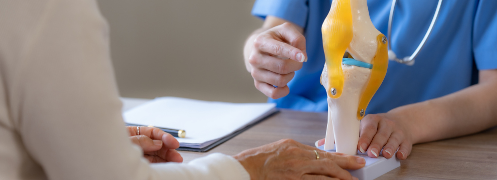 Un médico hablando con un paciente y haciendo gestos a un modelo de articulación de rodilla