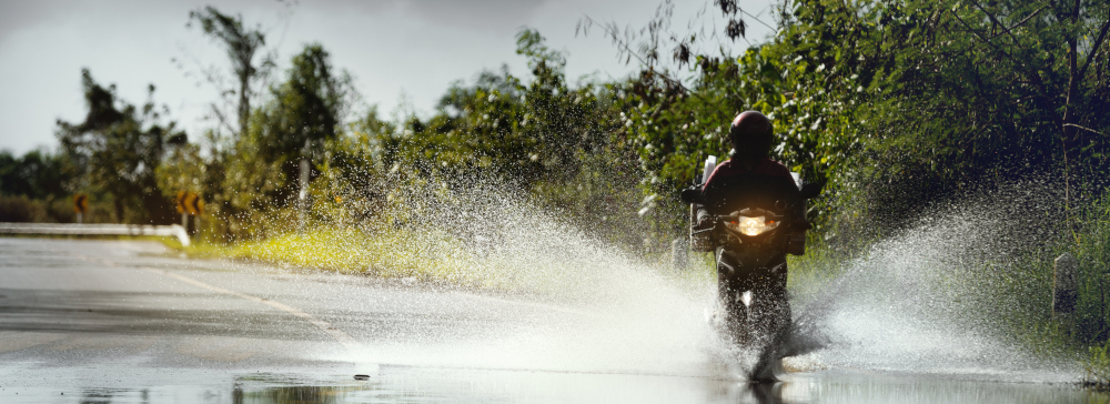 A motorcyclist driving through a flooded spot on the road after a storm.