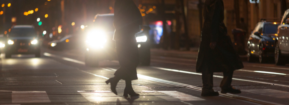 At night, pedestrians cross a bustling city street at a crosswalk.